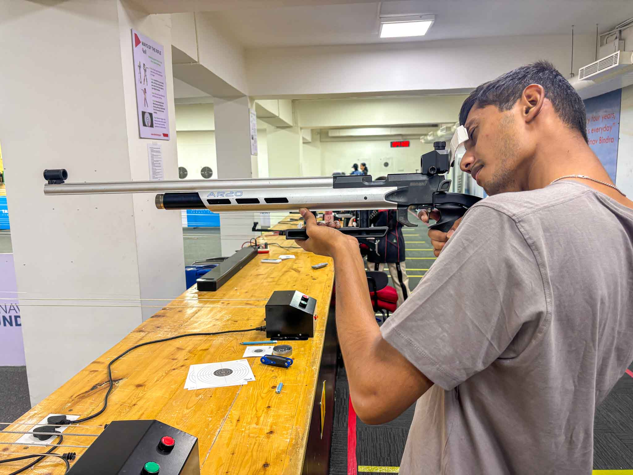 A young man aiming a rifle at a shooting range with focus and safety gear in Bengaluru's best shooting experience.